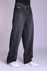 Front view of a person wearing oversized, dark grey acid-wash jeans and white sneakers against a plain background.