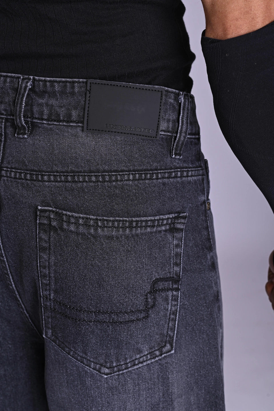 Close-up of dark grey acid-wash denim back pocket and waistband.