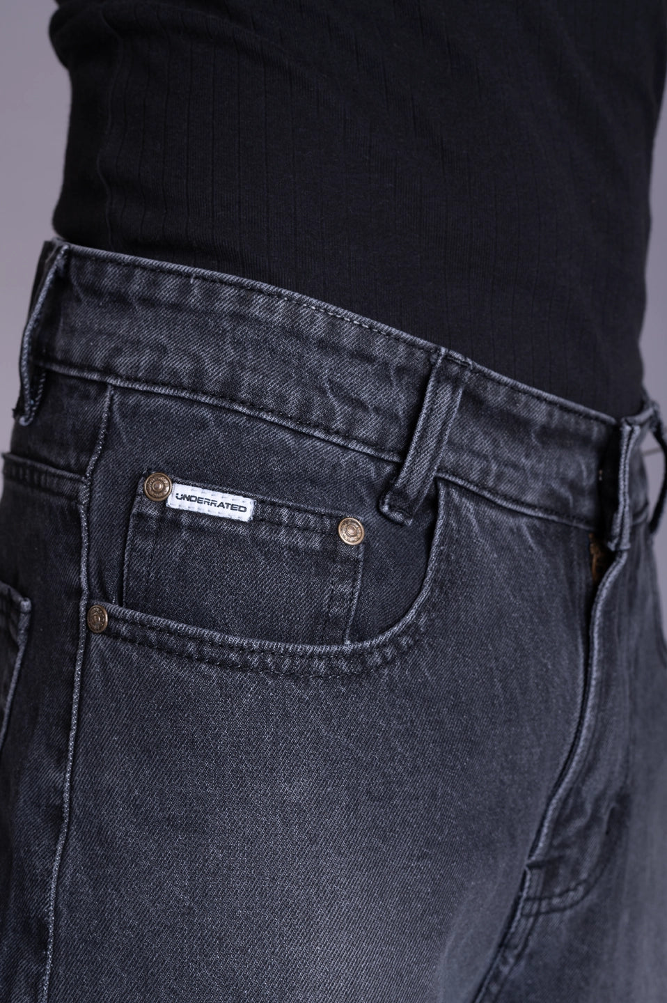 Front view close-up of dark grey acid-wash denim featuring a branded pocket tag.