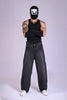 A tattooed man in a black tank top, arm sleeves, and a graphic balaclava wearing baggy charcoal acid-wash jeans.