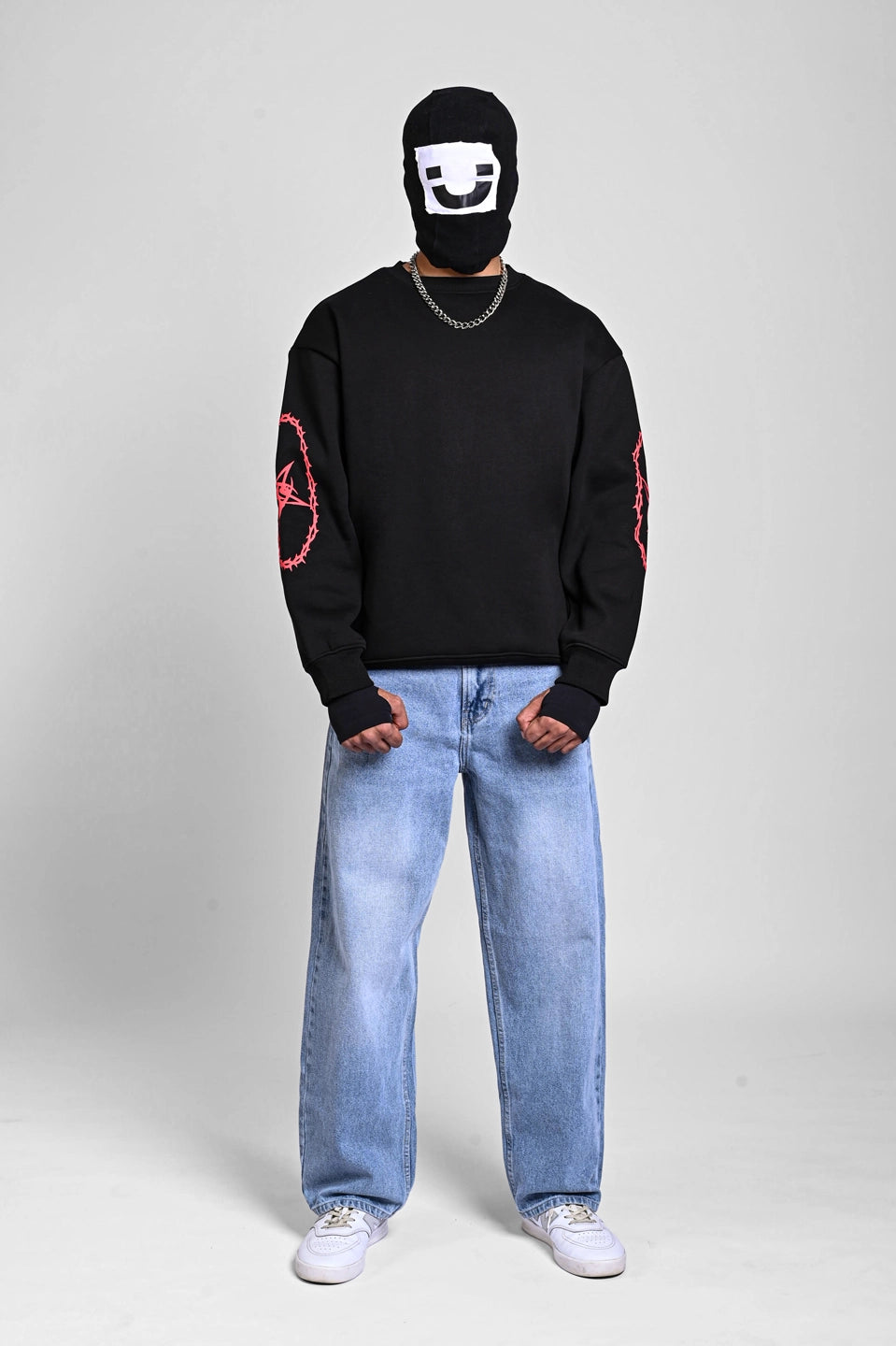 Front view of a person in a black sweatshirt with red thorny star graphics on the sleeves and a graphic balaclava.