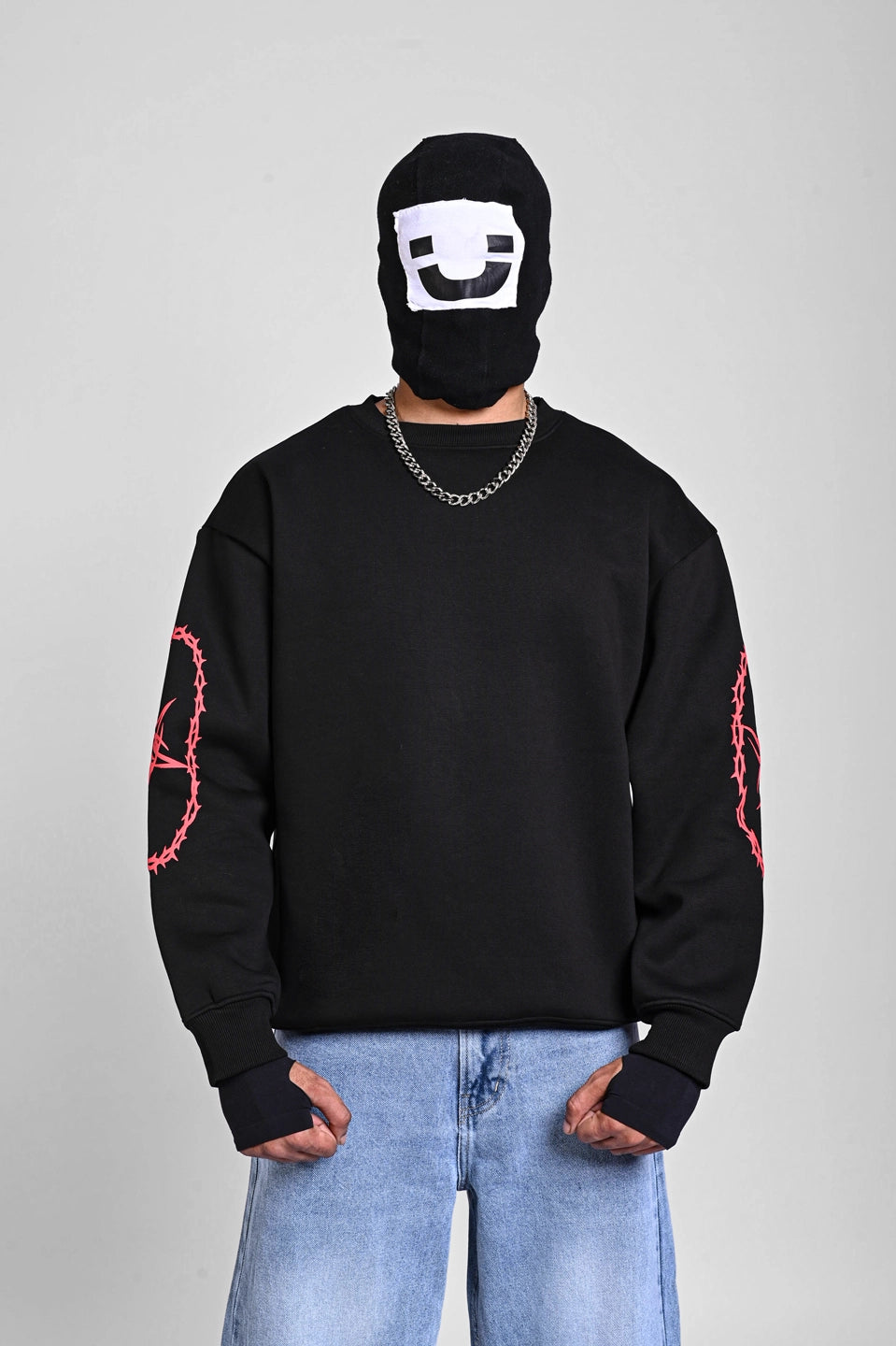 Front view of a person in a black sweatshirt with red thorny star graphics on the sleeves and a black face mask.