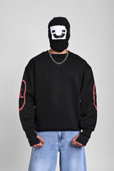 Front view of a person in a black sweatshirt with red thorny star graphics on the sleeves and a black face mask.