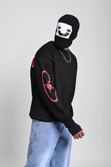 Side view of a person in a black sweatshirt with red thorny star sleeve graphics and a graphic balaclava.