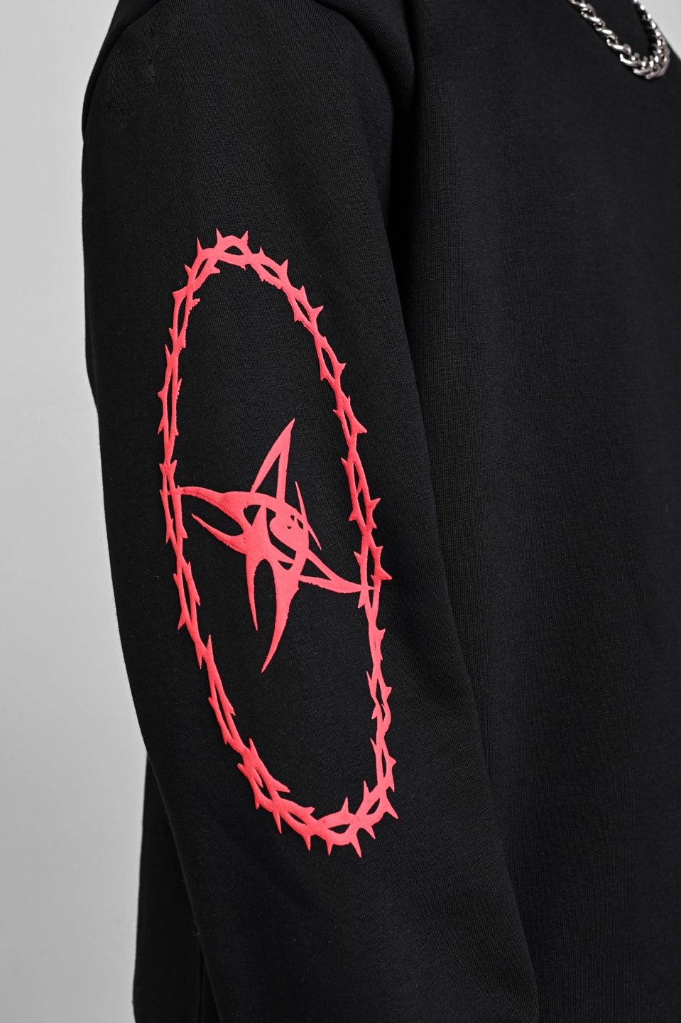 Close-up of a black sweatshirt sleeve featuring a red graphic of a star enclosed in a thorny oval frame.