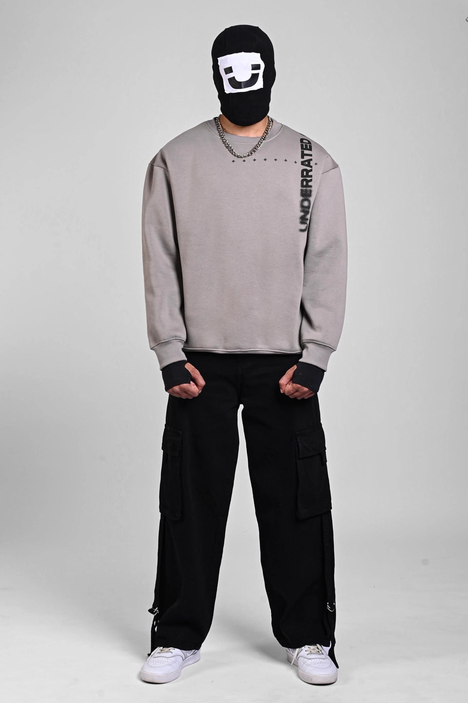 Front view of a person in a grey sweatshirt with vertical shoulder text, a silver chain, and a graphic balaclava.