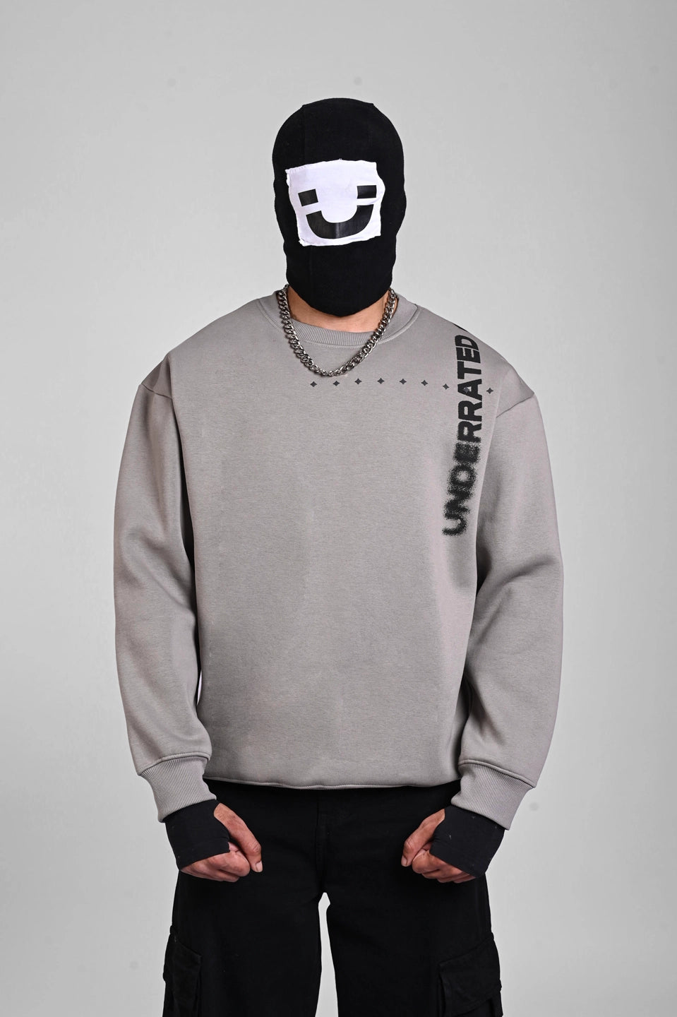Front view of a person in a grey sweatshirt with vertical shoulder text, a silver chain, and a graphic balaclava.