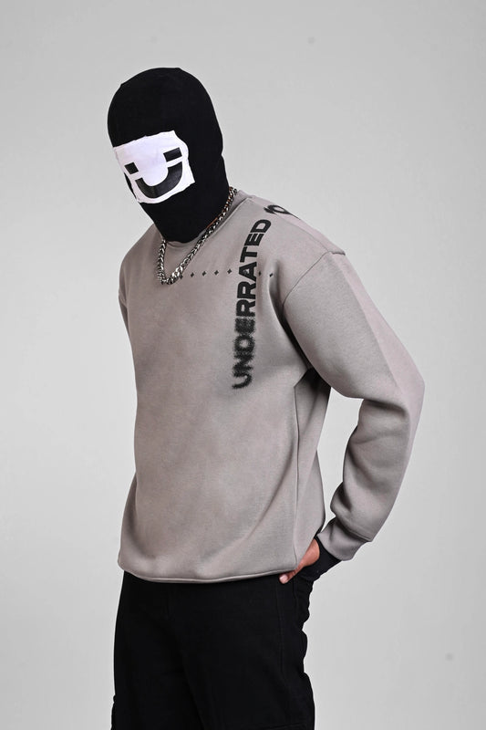 Side view of a person in a grey sweatshirt with vertical "UNDERRATED CLUB" text on the shoulder and a balaclava.