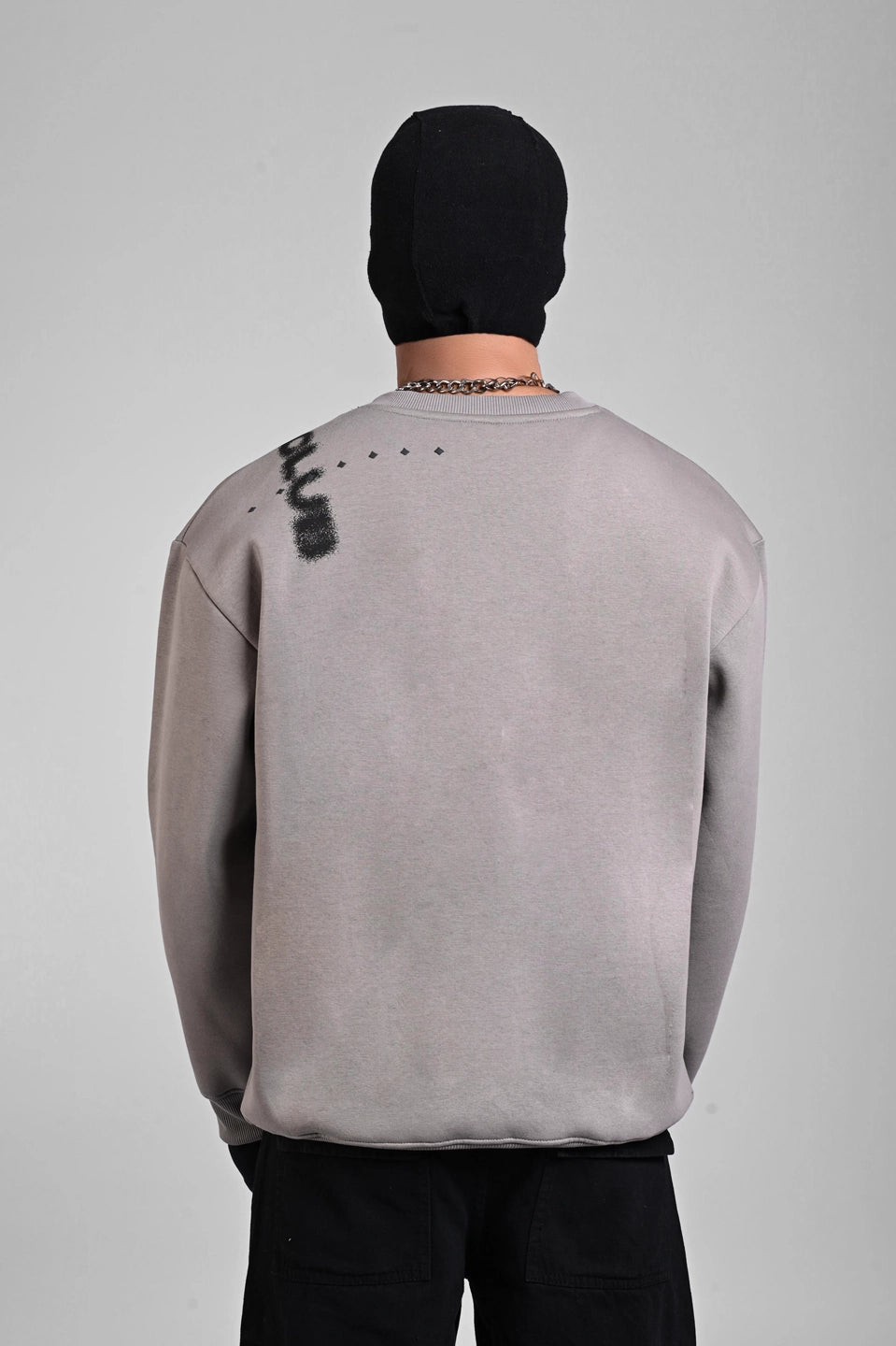 Back view of a person in a grey sweatshirt featuring vertical "UNDERRATED CLUB" text on the left shoulder.