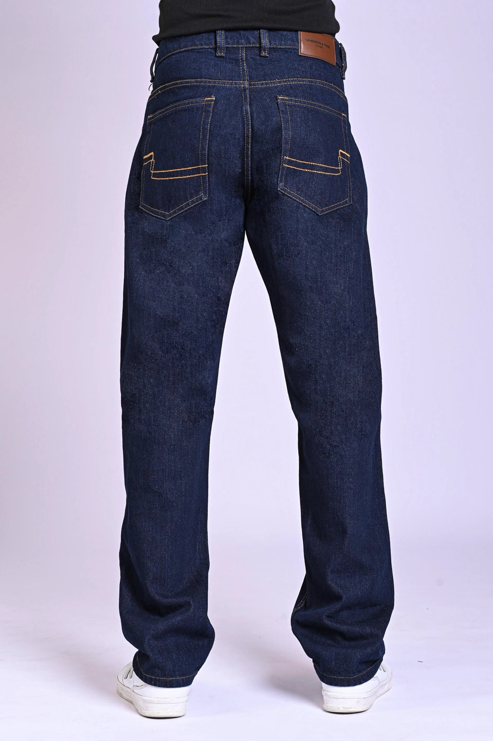 Back view of dark indigo blue jeans featuring a tan leather waist patch and curved pocket stitching.