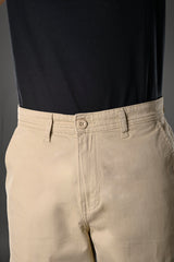 Close-up of beige UNDERRATED cargo pants waistband on model wearing black t-shirt, featuring button closure and drawstring details against grey background.
