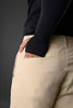Back view of beige UNDERRATED cargo pants on model in black long-sleeve top, hand in rear pocket, against grey background.

