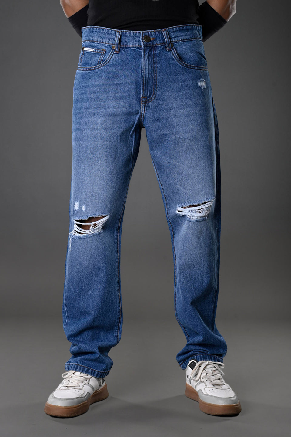 Underrated Club men's ripped distressed blue jeans knee rips slim fit model pose white sneakers urban fashion product photo.
