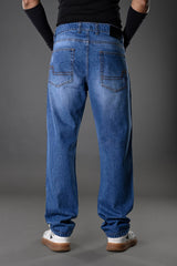 Rear full view man in light blue relaxed fit jeans black top arm cuffs white sneakers gray background Underrated Club denim.
