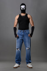 Full-body man wearing white smiley balaclava black tank top slim blue jeans white sneakers gray background.
