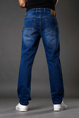 Full rear view man wearing blue distressed denim jeans white sneakers black top, showcasing back pockets stitching.
