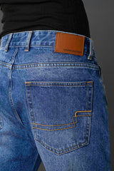 Close-up back pocket tan leather Underrated Club label yellow zigzag stitching light blue jeans detail.
