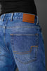 Close-up back pocket tan leather Underrated Club label yellow zigzag stitching light blue jeans detail.
