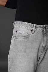 Underrated Club baggy jeans front pocket brass rivets light gray wash closeup branded apparel.
