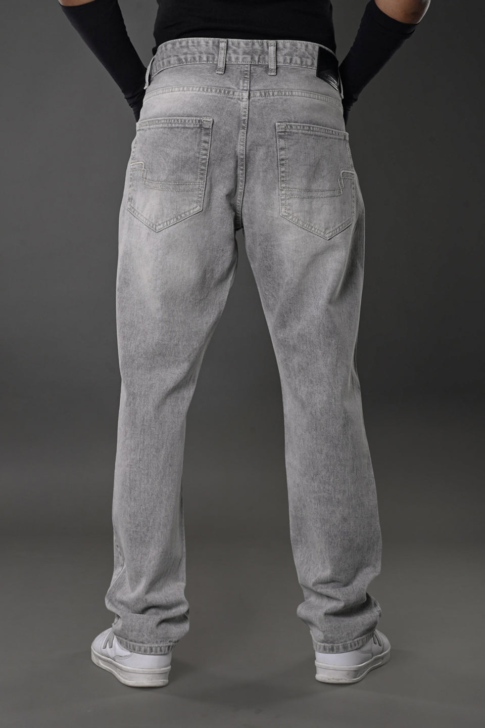 Men's grey baggy jeans full rear view model pose white sneakers gray background street style.
