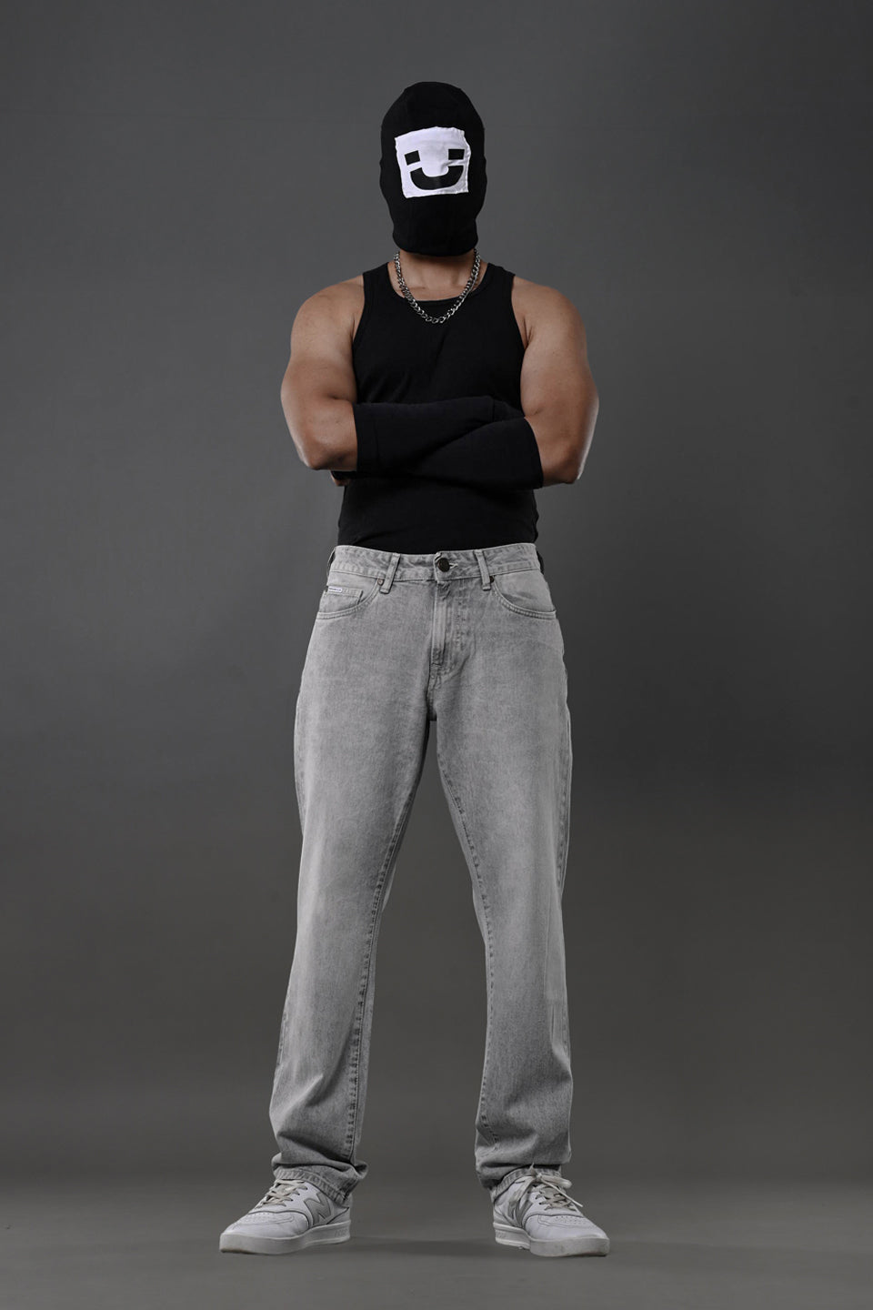 Underrated Club grey baggy jeans front model black balaclava tank top urban streetwear white sneakers.

