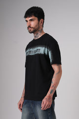 Side-angle view of the same black graphic t-shirt styled with blue jeans, showing the front chest print and the model’s tattooed arms.