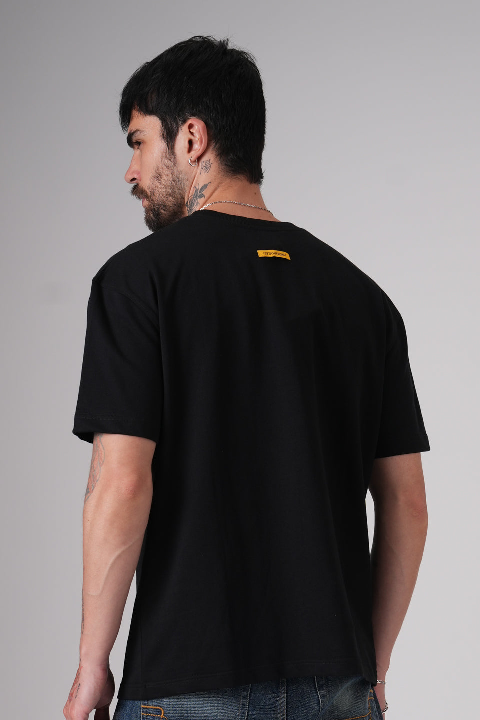 Close-up back view of the black t-shirt highlighting the plain rear with a small yellow label near the neckline.