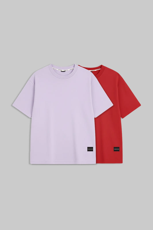 Two short-sleeve crewneck t-shirts displayed flat against a solid gray background. The front t-shirt is a light lavender purple, and the t-shirt behind it is a vibrant red.