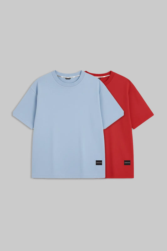 Two short-sleeve crewneck t-shirts displayed flat against a solid gray background. The front t-shirt is light blue, and the t-shirt behind it is red.