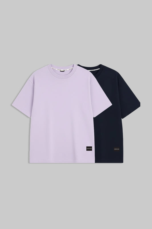 Two short-sleeve crewneck T-shirts displayed flat against a solid gray background. The front shirt is light lavender purple, and the shirt behind it is dark navy blue.