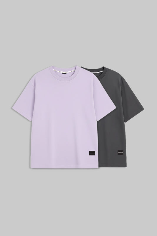 Two short-sleeve crewneck t-shirts displayed against a solid gray background. The front t-shirt is a light lavender purple, and the t-shirt behind it is dark charcoal gray.