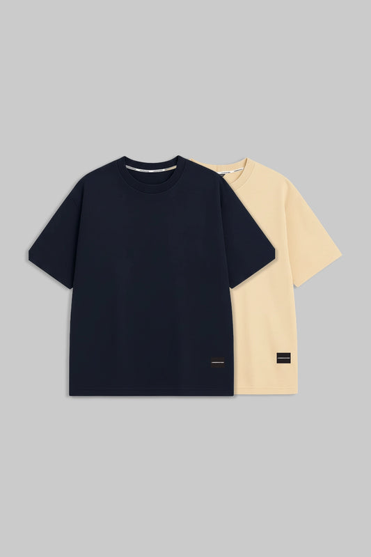 Two short-sleeve crew-neck t-shirts displayed flat against a solid gray background. The front t-shirt is dark navy blue, and the t-shirt behind it is light cream/beige.
