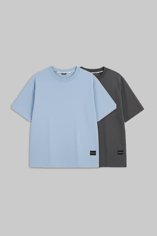 Two short-sleeve crewneck t-shirts displayed against a solid gray background. The front t-shirt is light blue, and the t-shirt behind it is dark gray.