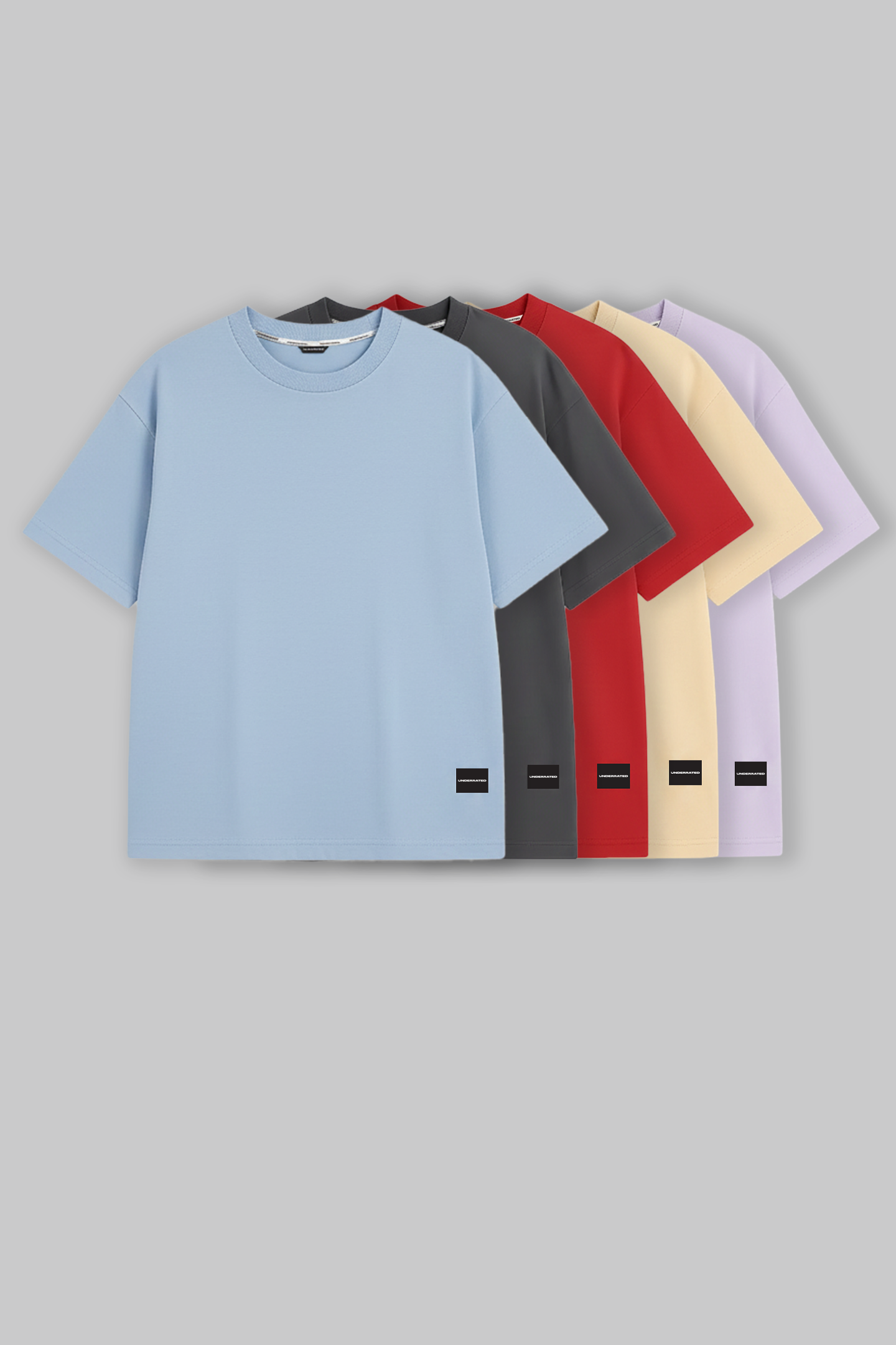 UNDERRATED oversized t-shirts quintet in light blue, grey, red, beige, and lavender colors with brand tags against grey background - men's streetwear collection.
