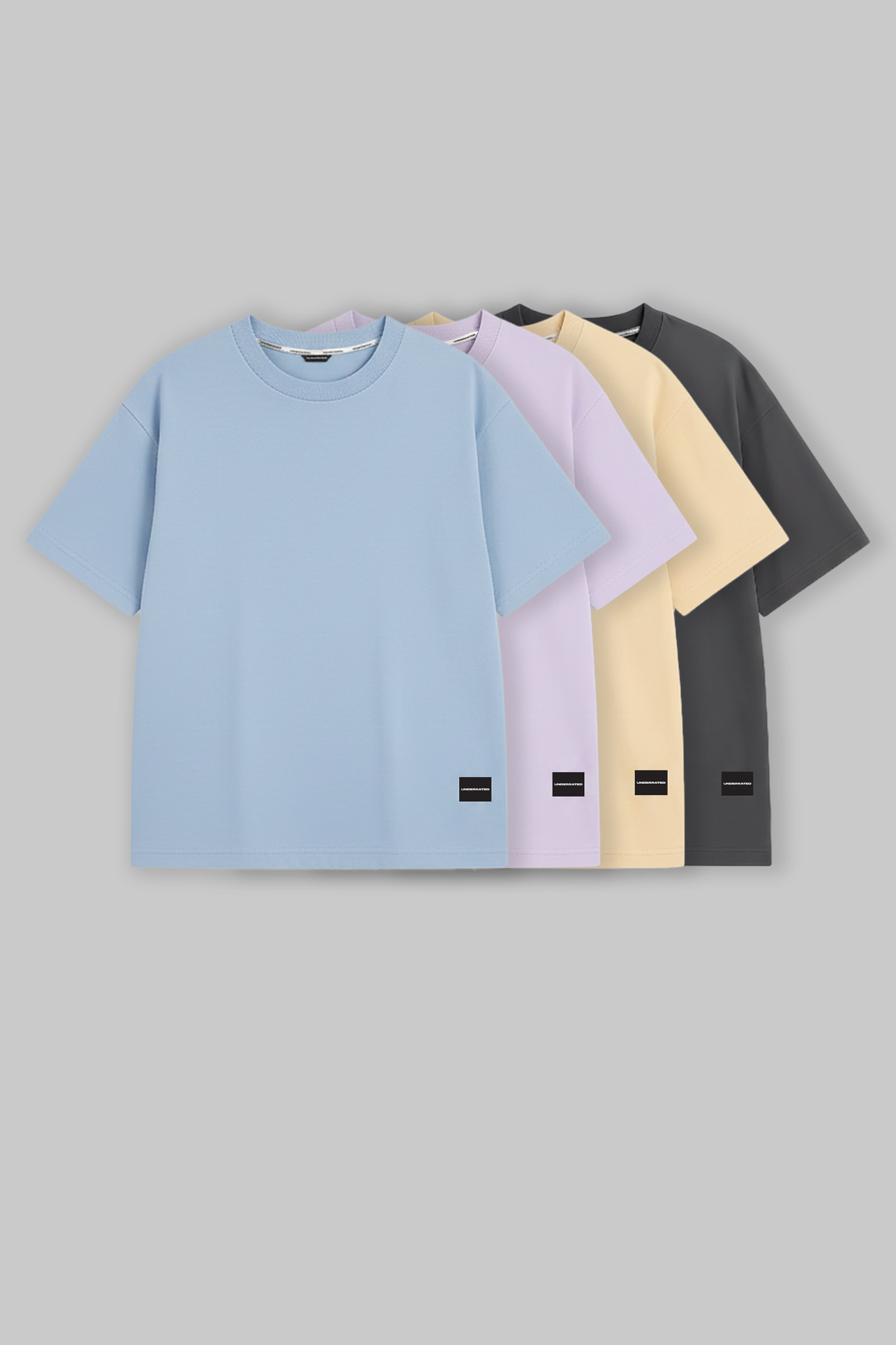 UNDERRATED oversized t-shirts quartet in light blue, lavender, beige, and grey colors with brand tags against grey background - men's streetwear essentials.
