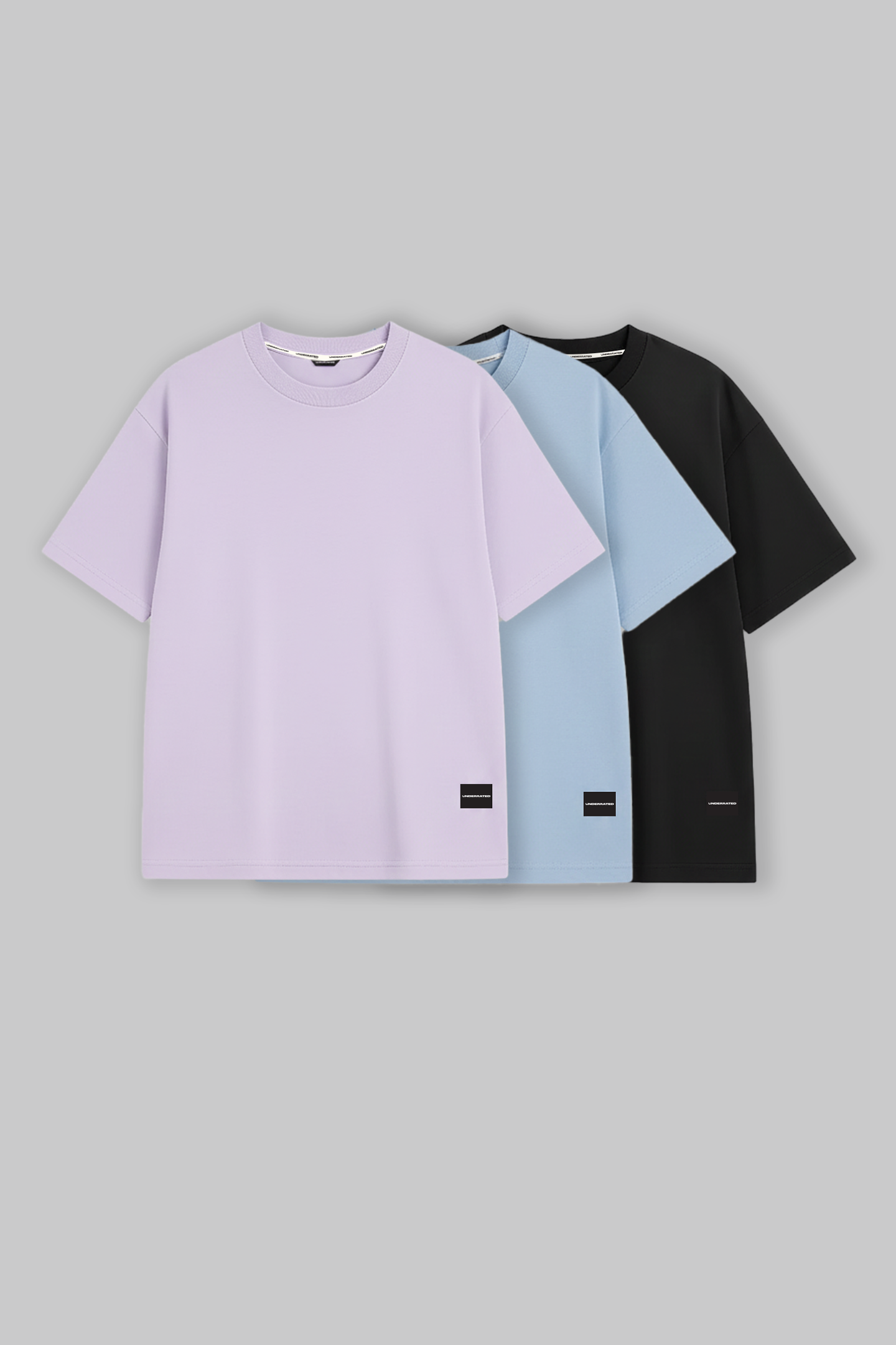 UNDERRATED oversized t-shirts trio in lavender, light blue, and black colors with brand tags against grey background - men's streetwear basics.