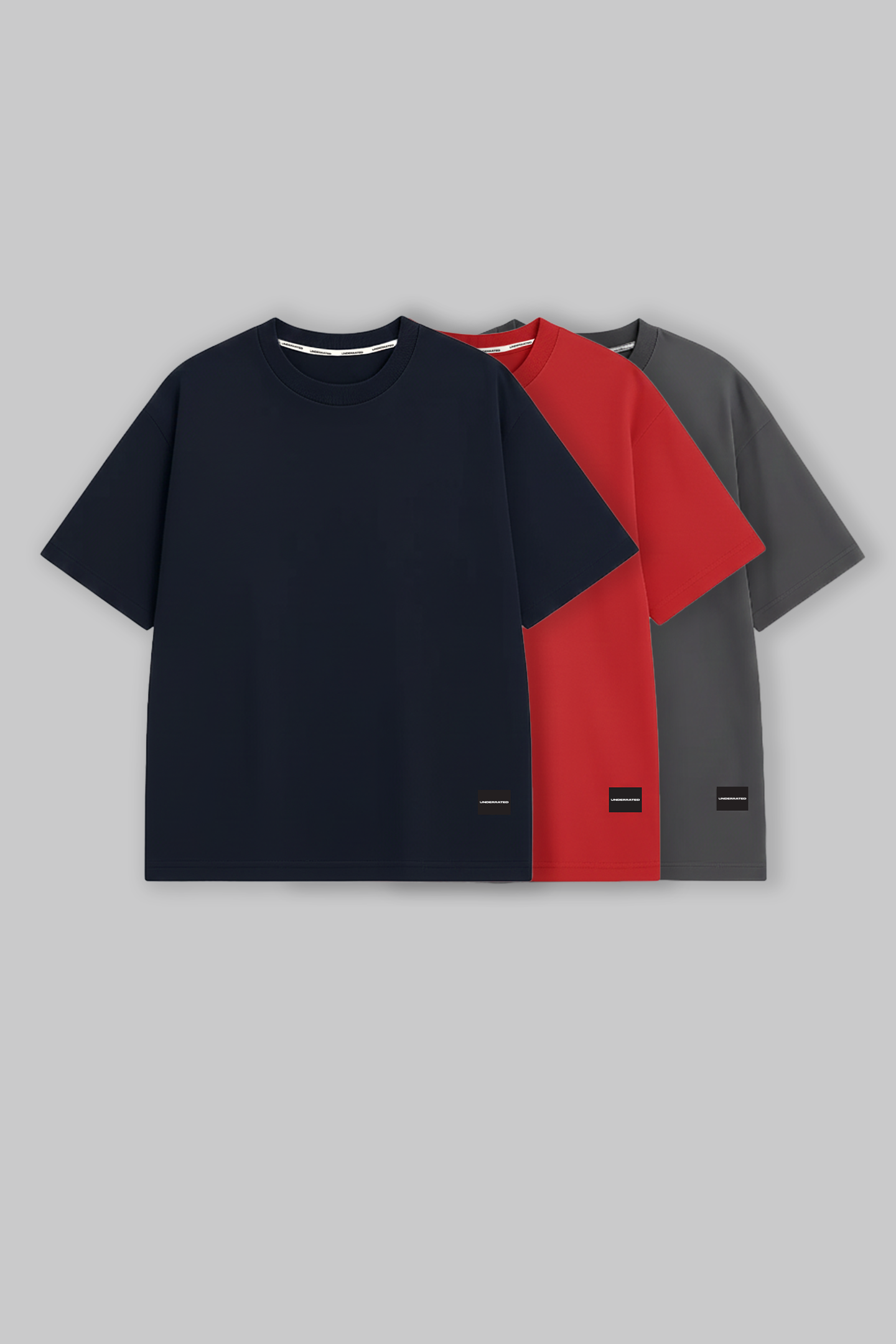 UNDERRATED oversized t-shirts trio in navy blue, red, and grey colors with brand tags against grey background - men's streetwear essentials.

