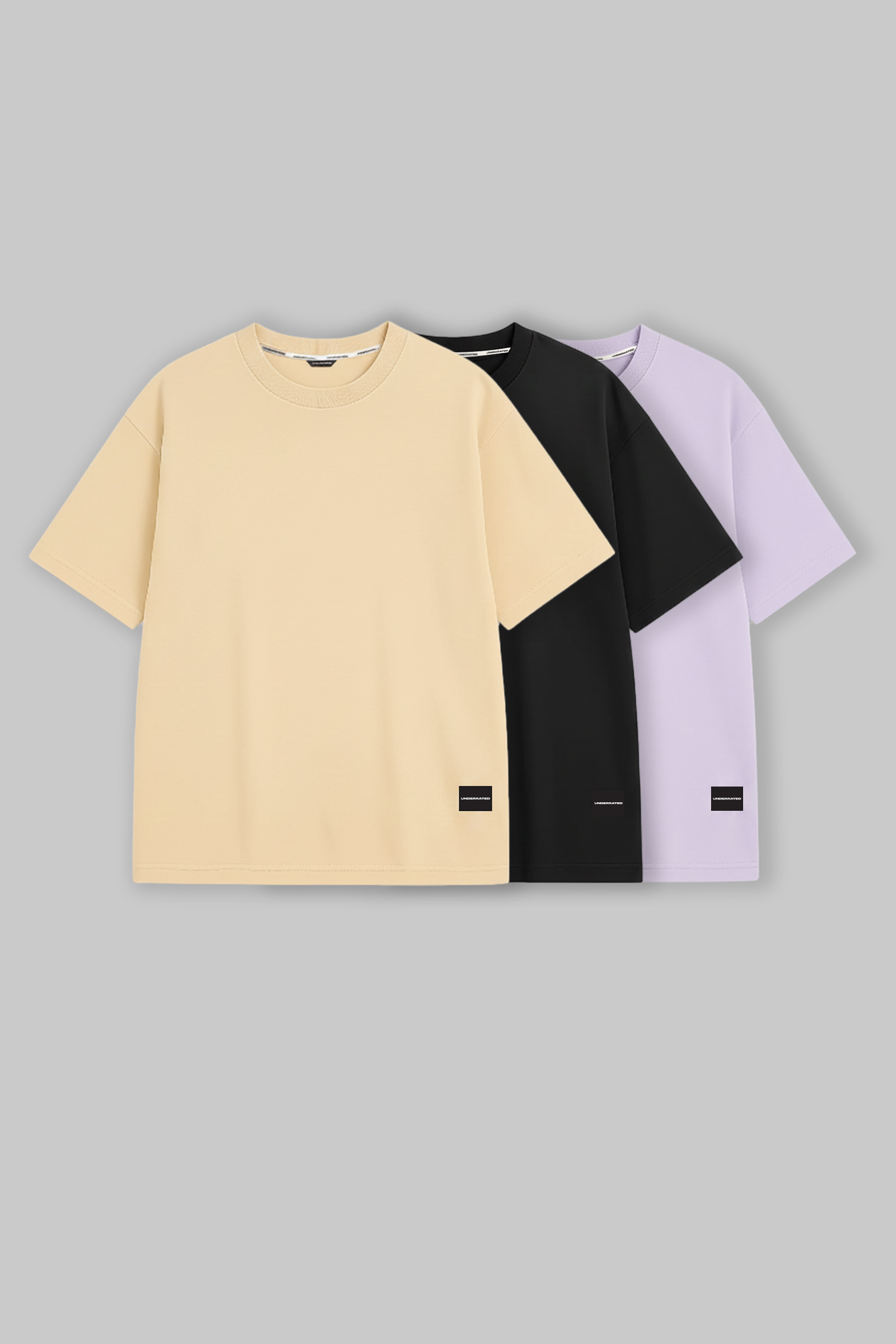 UNDERRATED oversized t-shirts trio in beige, black, and lavender colors with brand tags against grey background - men's streetwear essentials.
