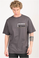 A young man with curly blonde hair wearing a charcoal gray oversized t-shirt with a rectangular graphic on the chest that includes the words 