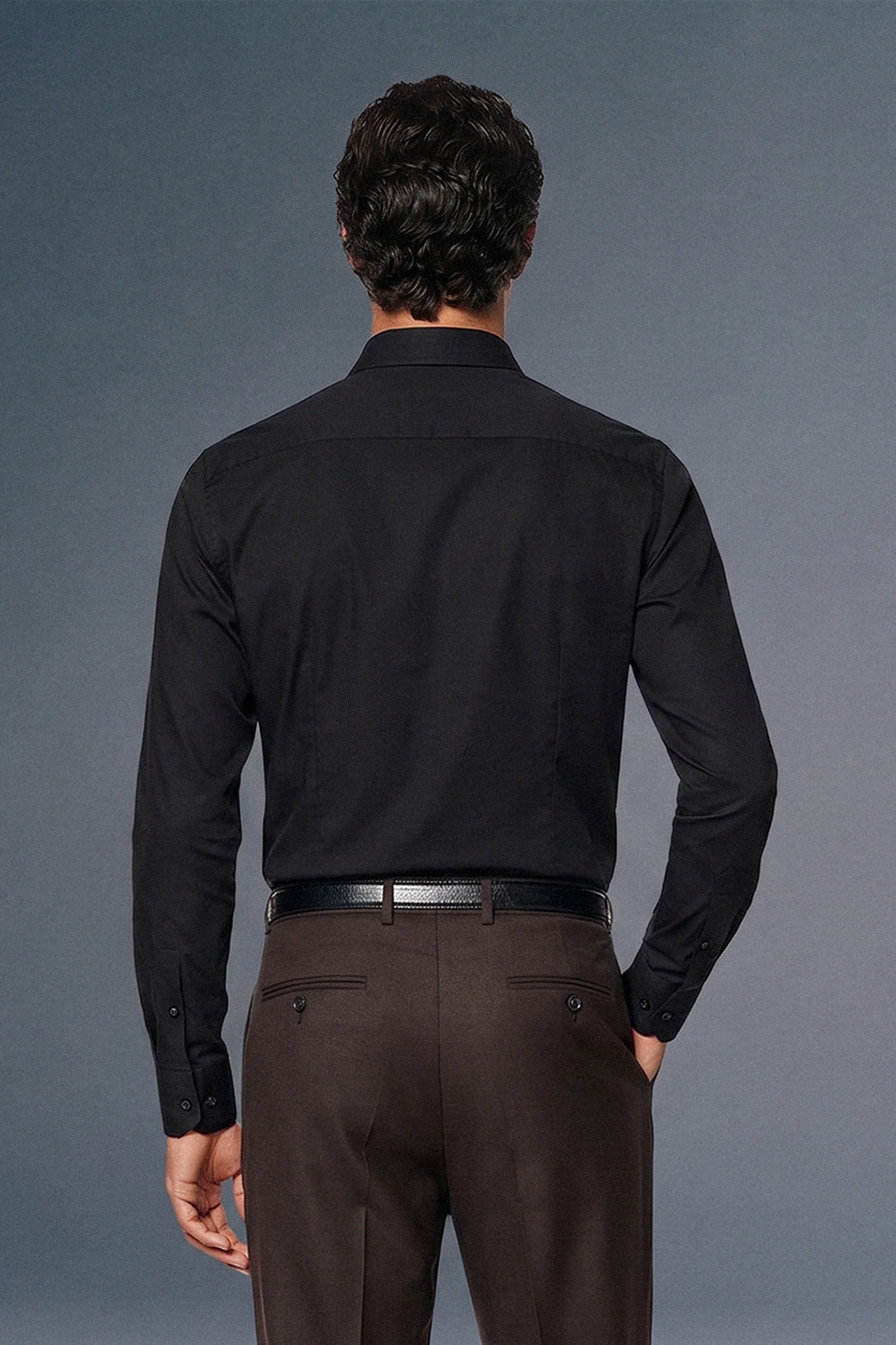 Man wearing a black dress shirt and brown pants against a gray background