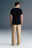 Full-length rear view of a man standing straight, wearing a black polo shirt with a beige collar and patterned sleeve trim, paired with khaki trousers.