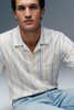 Man wearing a striped shirt and jeans against a gray background