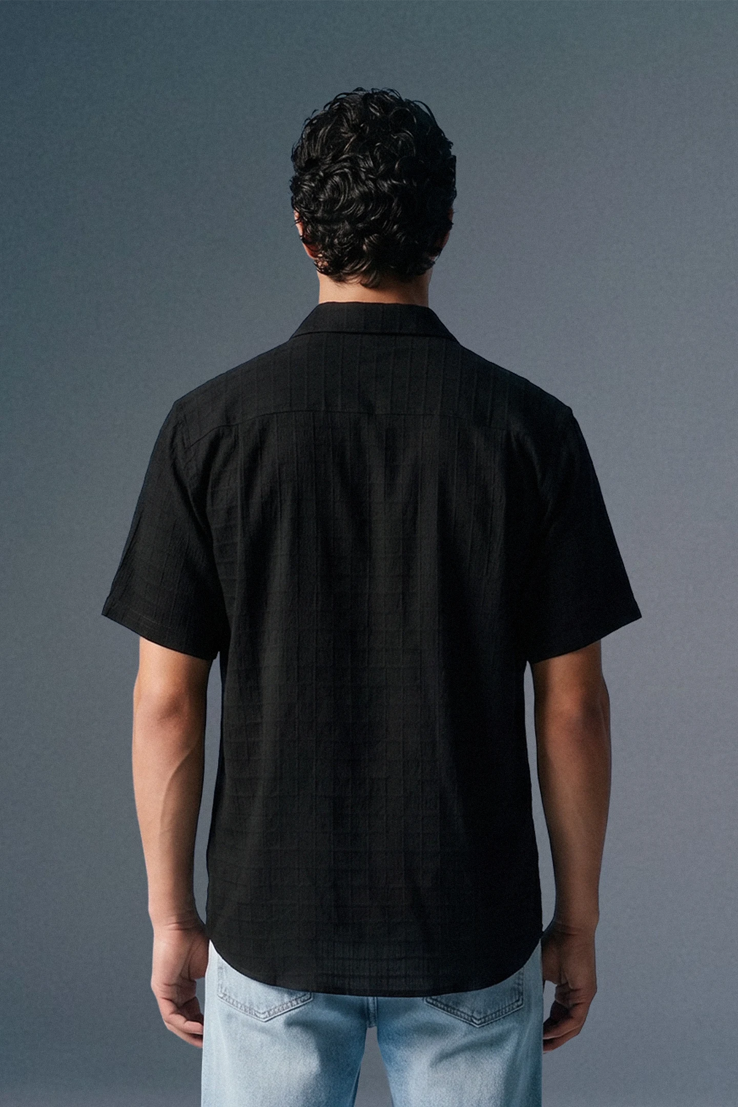 Person wearing a black shirt and light blue jeans against a gray background
