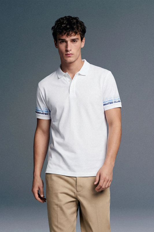 A three-quarter front shot of a man standing still, wearing a white polo shirt with blue cuff detailing paired with khaki pants.