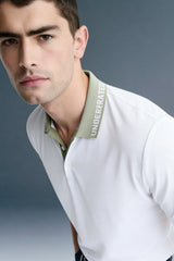 A close-up, angled dynamic shot from the chest up of a man leaning forward, highlighting the olive green collar and button placket of a white polo shirt.