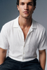 Man wearing a white checkered shirt with short sleeves against a gray background