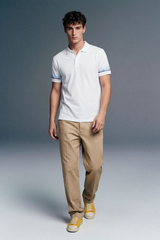 Full-length front view of a man walking forward, wearing a white polo shirt with blue-patterned cuffs, beige trousers, and yellow shoes against a grey gradient studio background.