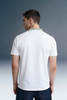 Rear view from the waist up of a man looking over his left shoulder, showing the back of a white polo shirt with a contrasting olive green collar.