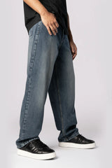 Side view of a person in baggy blue denim jeans and black shoes with thick white soles.