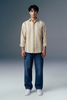 Man wearing a beige striped shirt and blue jeans against a gray background